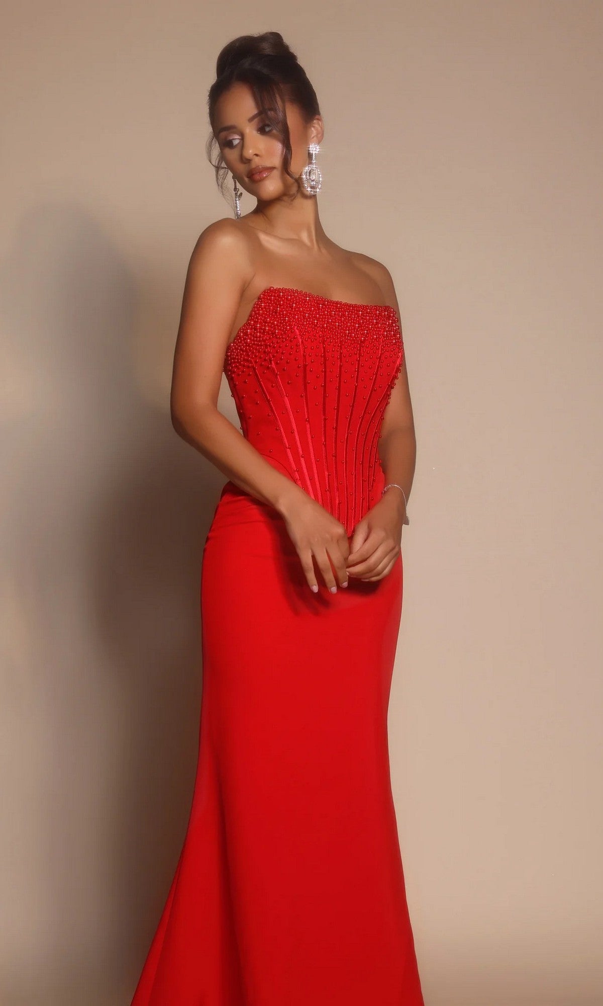 A woman models the Portia and Scarlett PS26008 long formal dress, showcasing its strapless beaded corset bodice and fitted red floor-length skirt against a plain background.